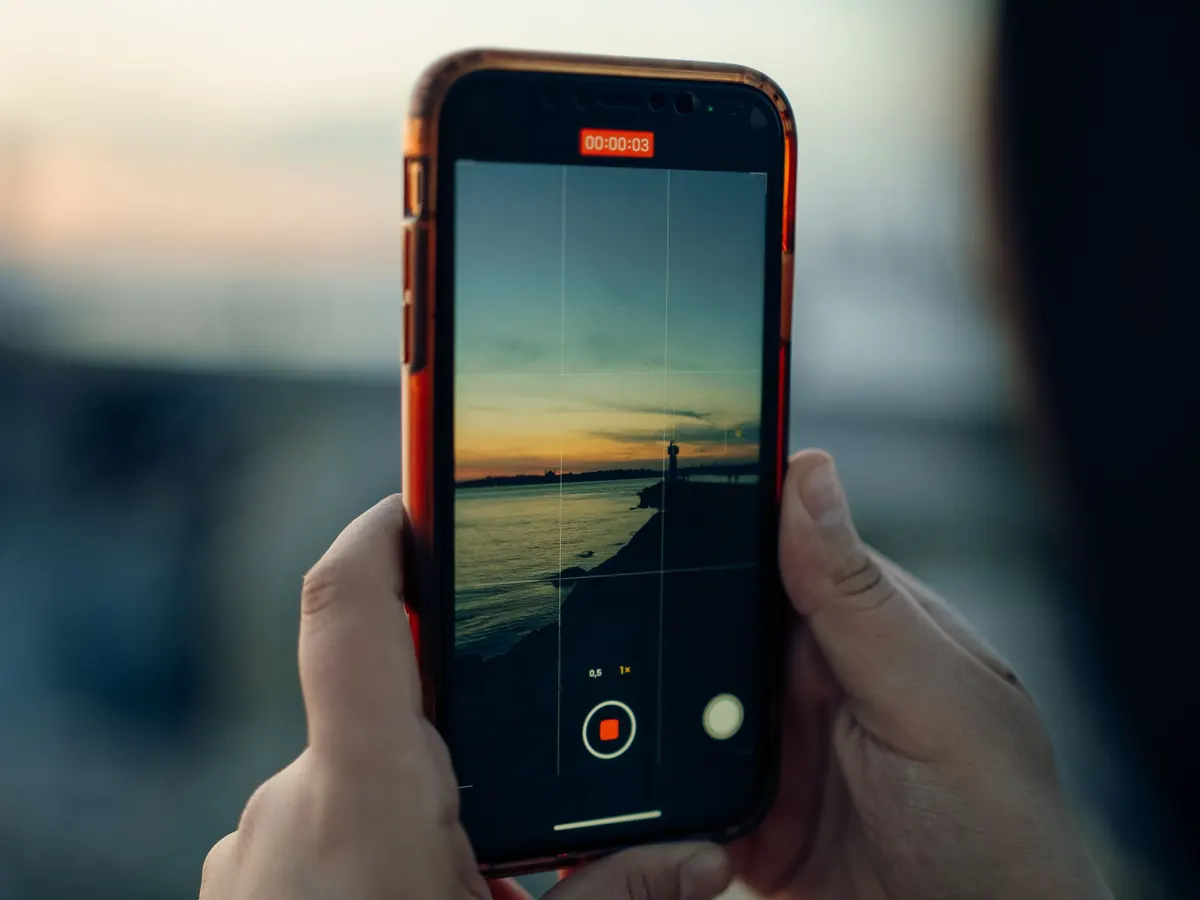 Two hands holding a phone that is recording a video of a sunset over the water
