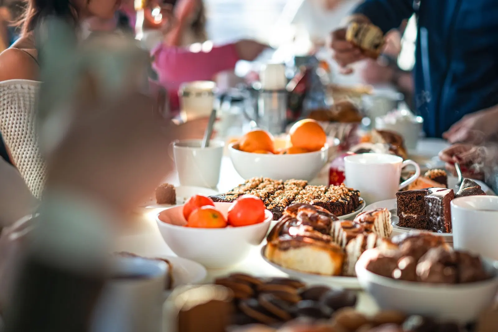 Cups of tea, slices of cake and bowls of mandarins on a long shared table as people help themselves