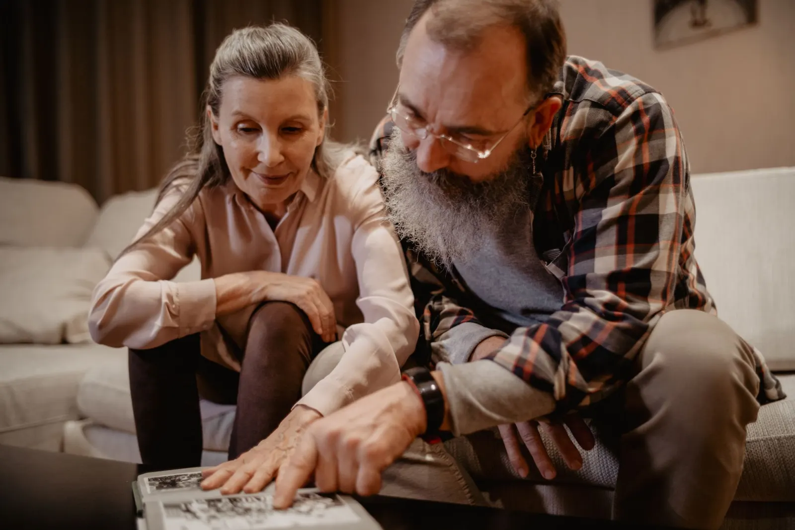 An older couple sit on a sofa and turn the pages of a black-and-white photo album together